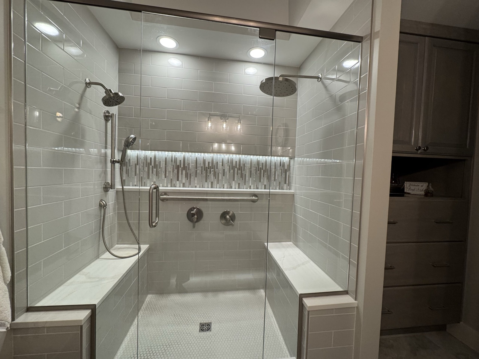 Walk-in shower with lit tile niche, bench, and glass door